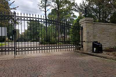 Completed driveway gates project with stone wall pillars and a brick driveway.